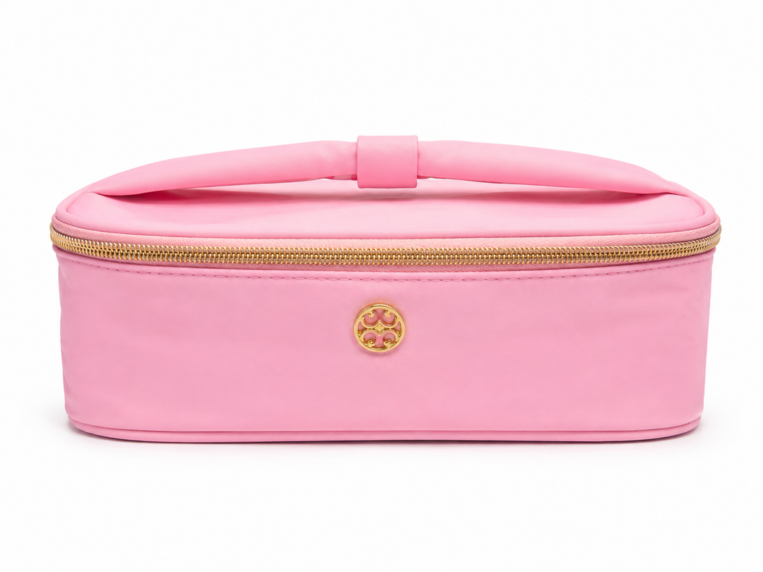 Pink cosmetic travel case with gold zipper, top handle, and structured design for makeup, toiletries, and beauty essentials.