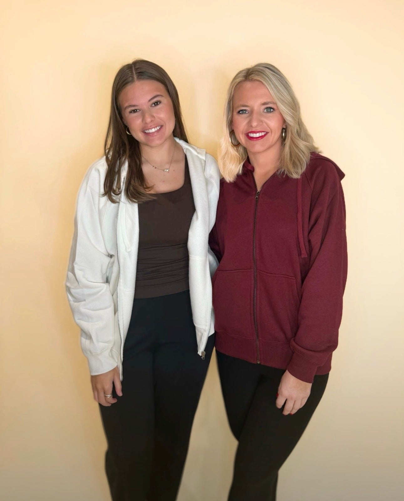Two women wearing zip-up hoodies, one in ivory and one in maroon, styled with black pants for casual everyday look.
