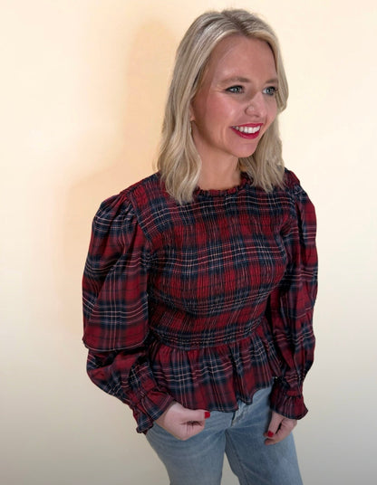 Red and navy plaid long sleeve top with smocked waist and puff sleeves shown from a front-side angle, styled with denim for a casual holiday look.