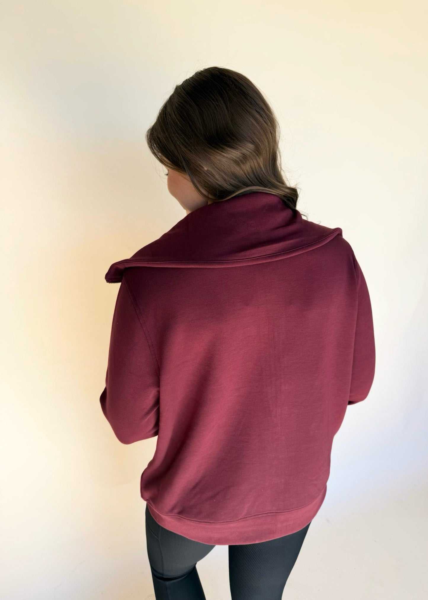 Person wearing a maroon jacket from behind on a plain background