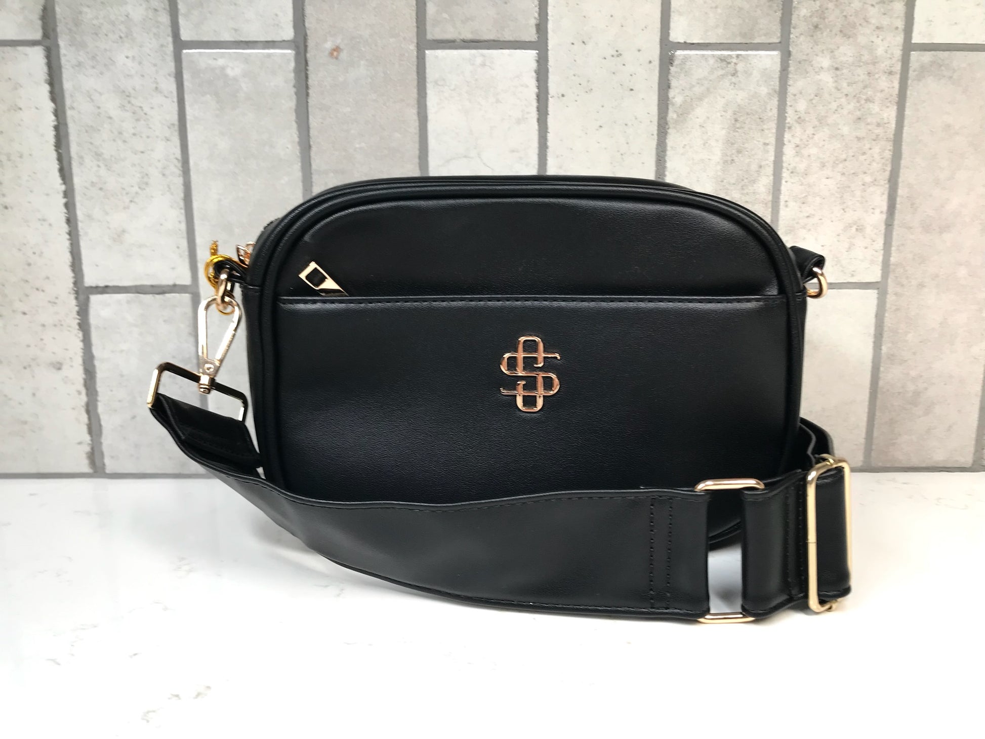 Black shoulder bag with gold accents on a tiled floor background