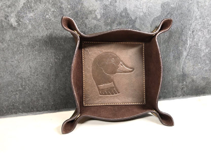 Brown leather tray with embossed dog design on a gray background