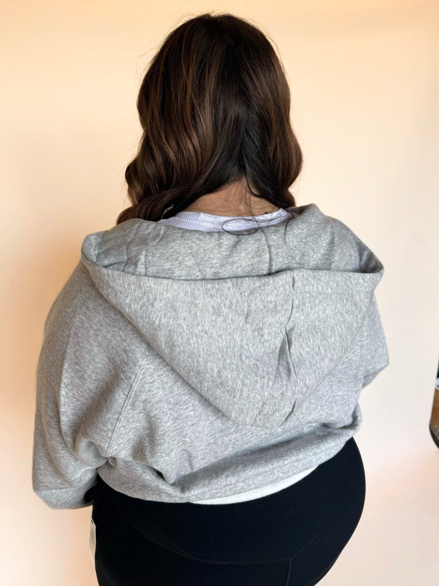 Back view of a woman wearing a light gray zip-up hoodie, showing the hood and relaxed fit.