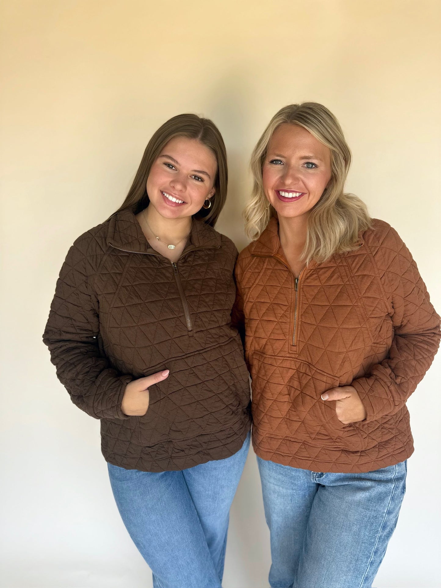 Two women wearing brown quilted jackets standing against a plain background