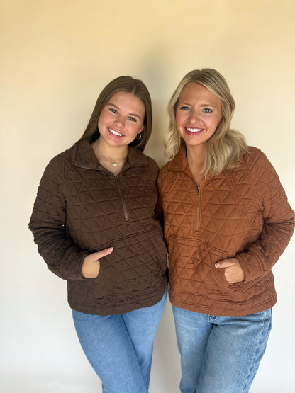 Two women wearing brown quilted jackets standing against a plain background
