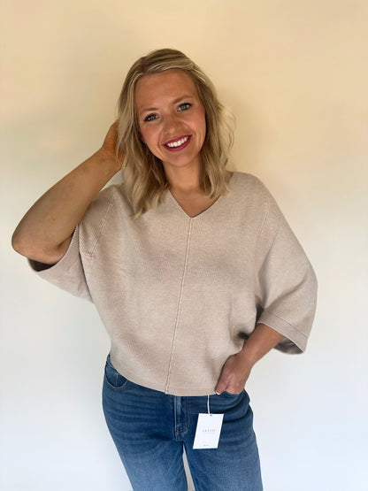 Woman wearing an oatmeal sweater and blue jeans with a white background