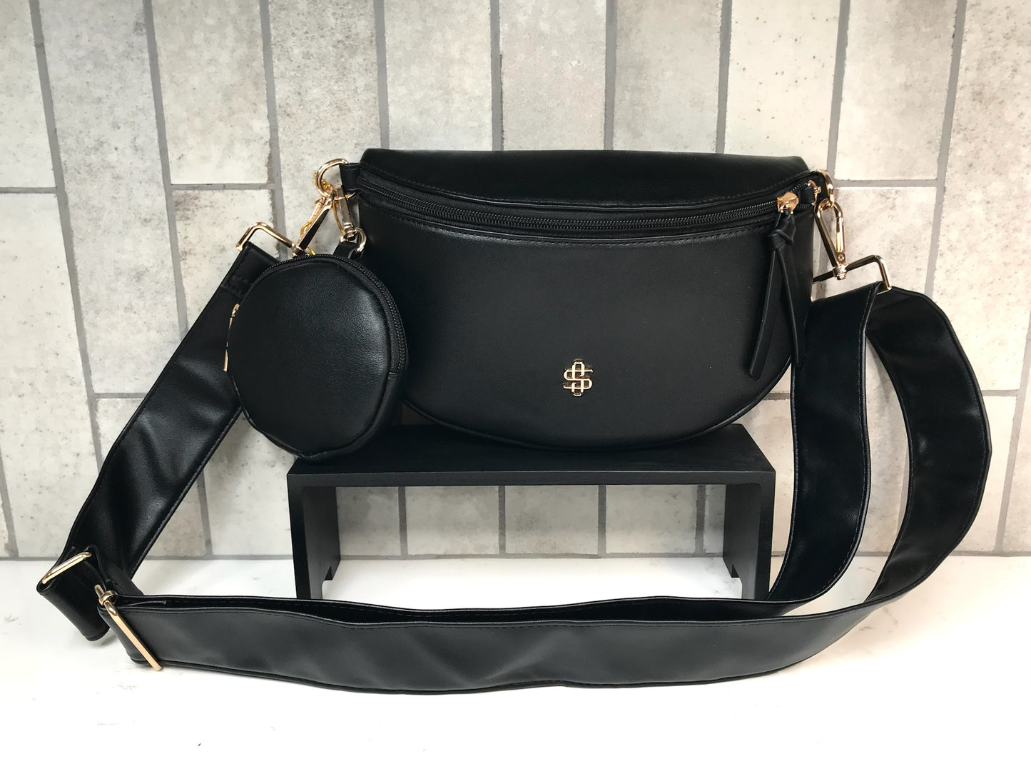 Black handbag with a smaller round bag on a stand against a tiled wall background