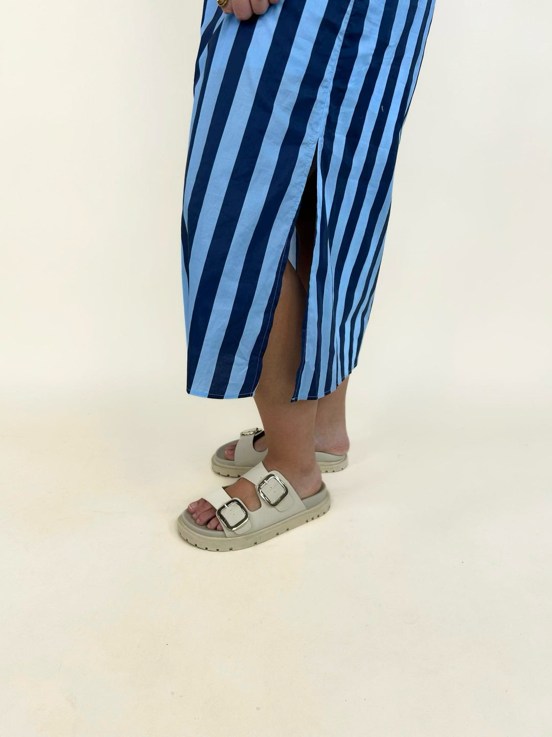 Close-up of the blue striped midi shirt dress featuring a side slit and lightweight woven fabric, styled with cream double-buckle platform sandals.