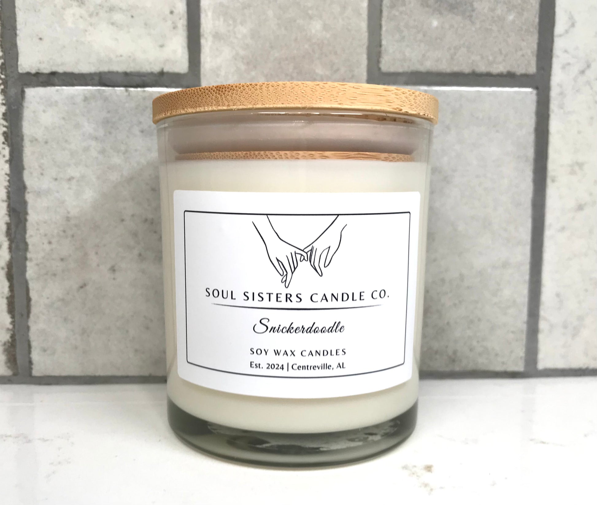 Scented candle with a wooden lid on a white surface against a gray tiled wall.