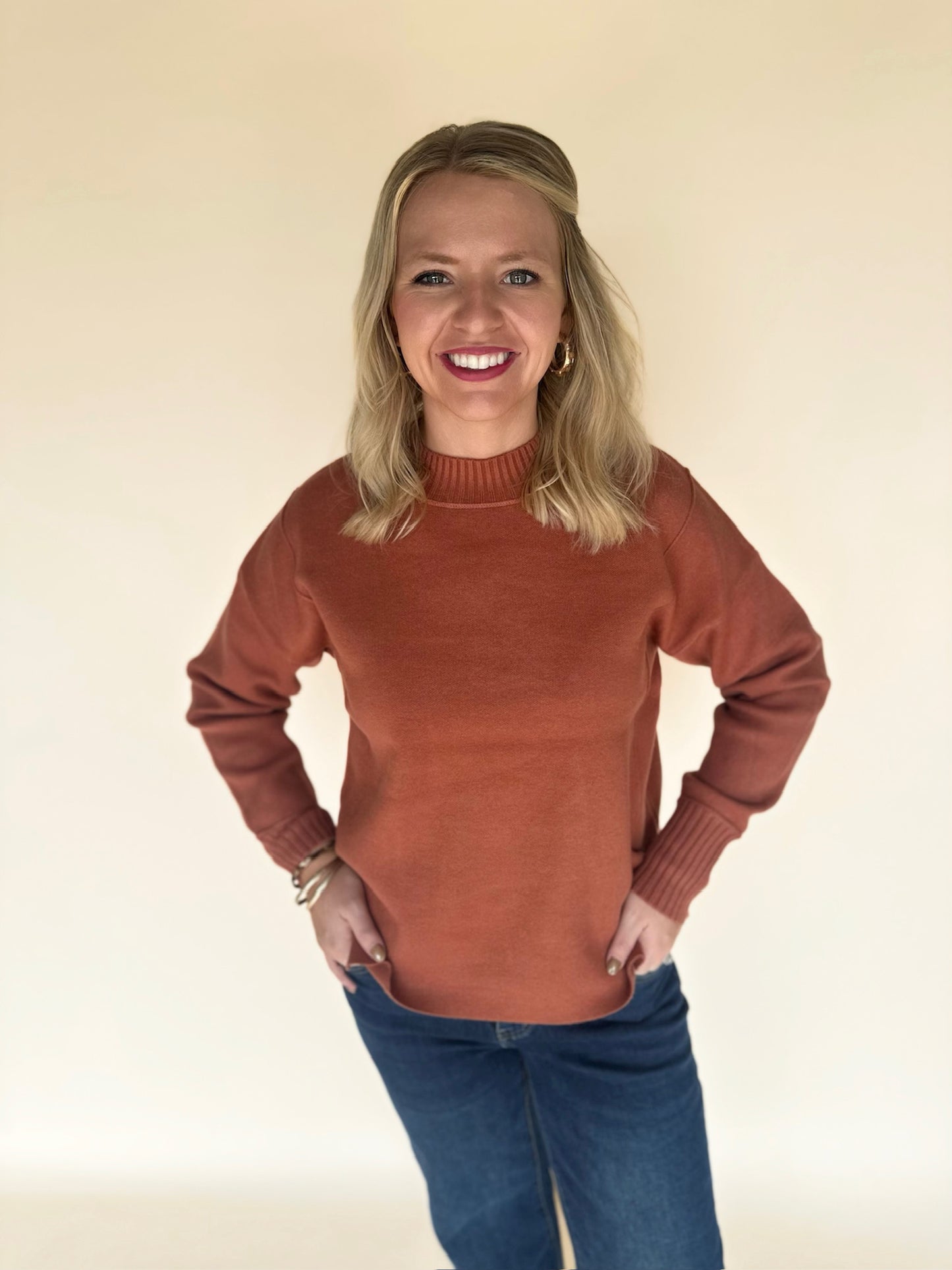 Woman wearing a copper sweater and blue jeans against a beige background