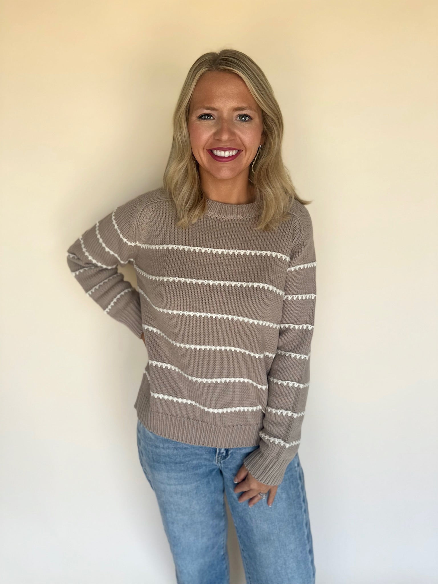 Woman wearing a striped sweater and jeans against a plain background