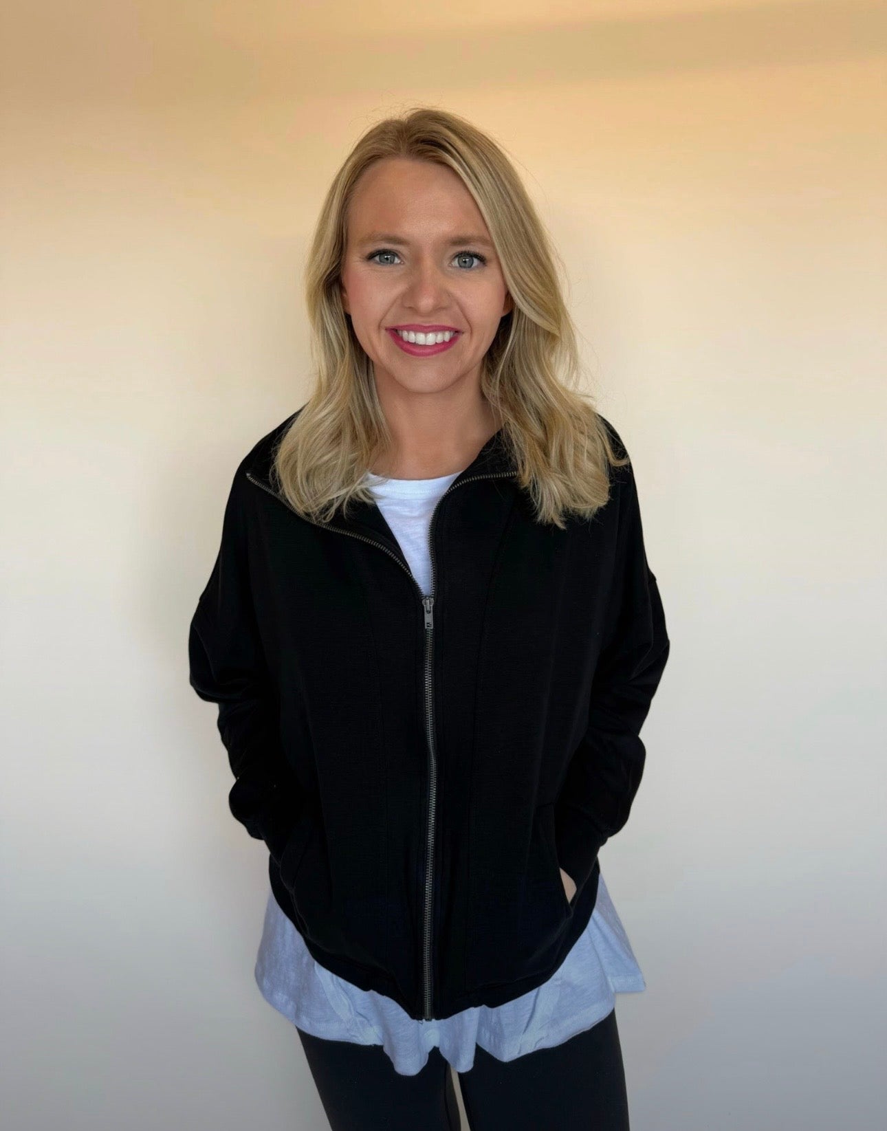 Woman wearing a black jacket over a white shirt with a plain background
