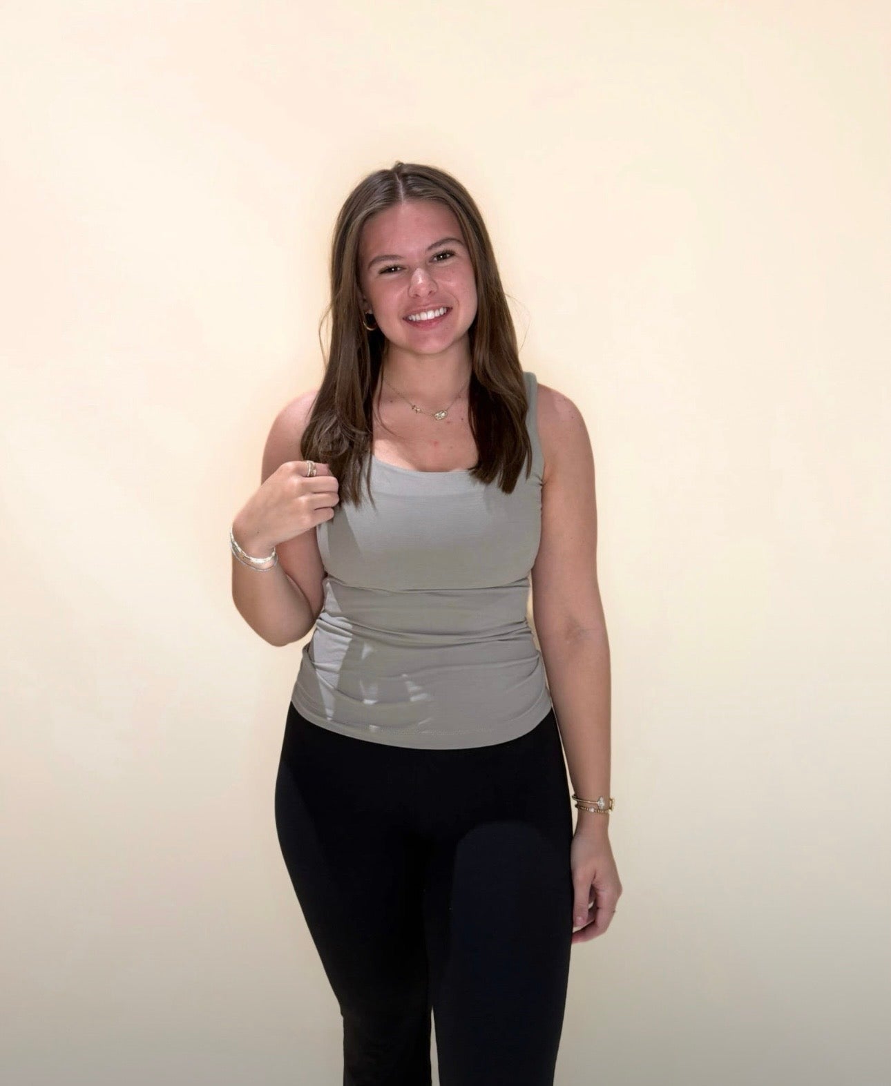 Young woman modeling a taupe fitted tank top with black leggings, posing with a light neutral background.