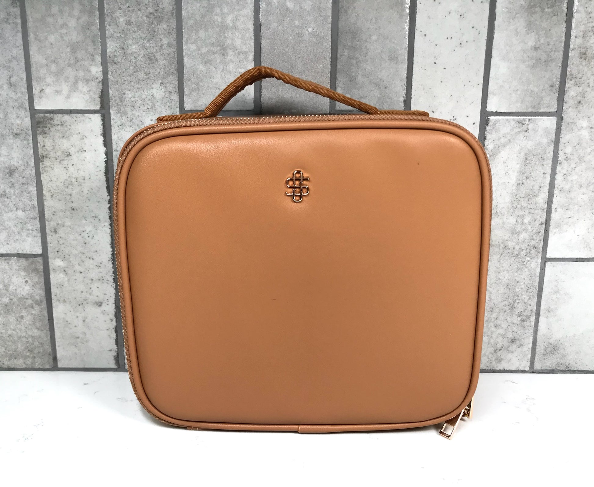 Brown leather cosmetic case with a visible brand logo on a gray tiled background