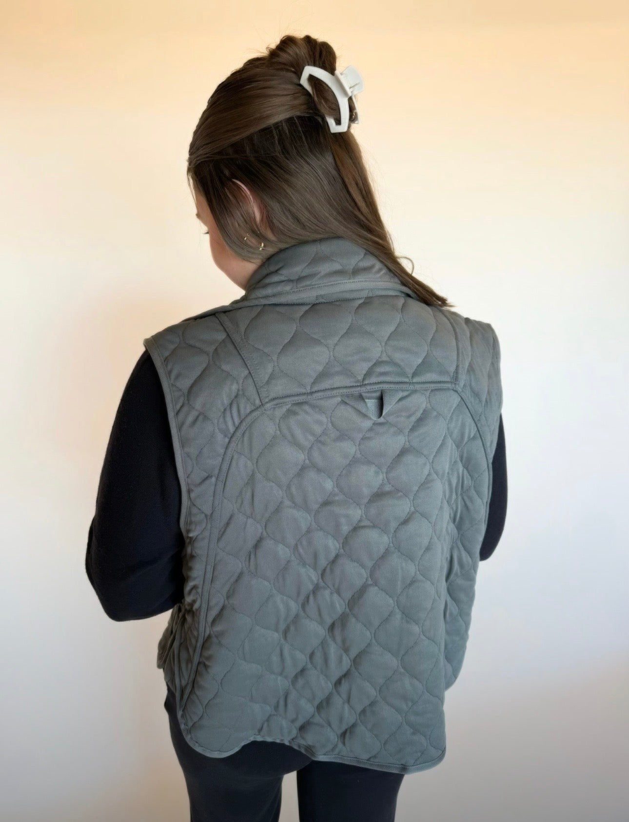 Person wearing a gray quilted vest against a plain background