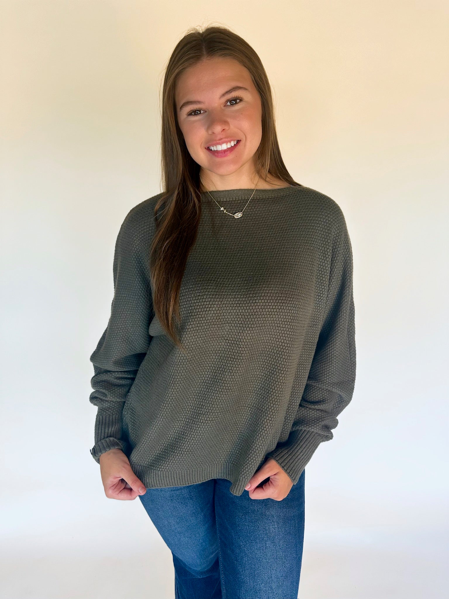 Woman wearing a green sweater and blue jeans against a plain background