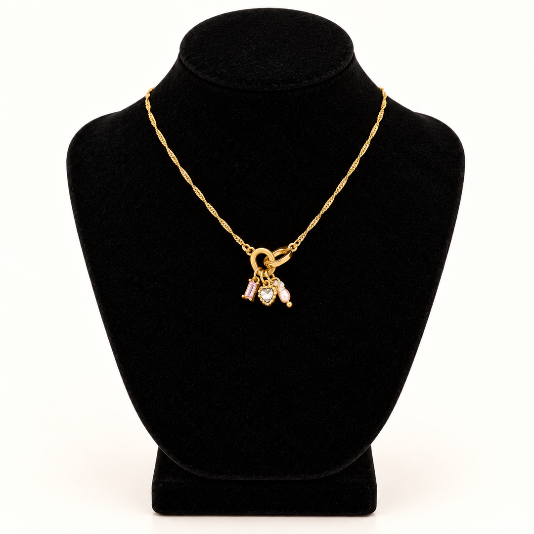 Jane Marie 16-inch gold chain necklace with petite 0.5-inch pink crystal and heart charm pendant cluster displayed on a black velvet necklace bust against a cream background.