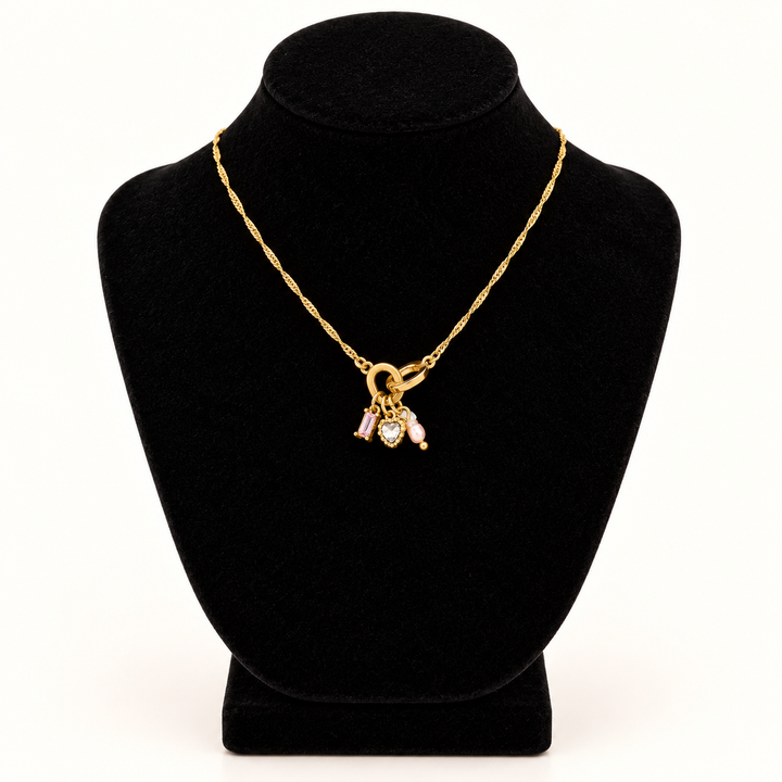 Jane Marie 16-inch gold chain necklace with petite 0.5-inch pink crystal and heart charm pendant cluster displayed on a black velvet necklace bust against a cream background.