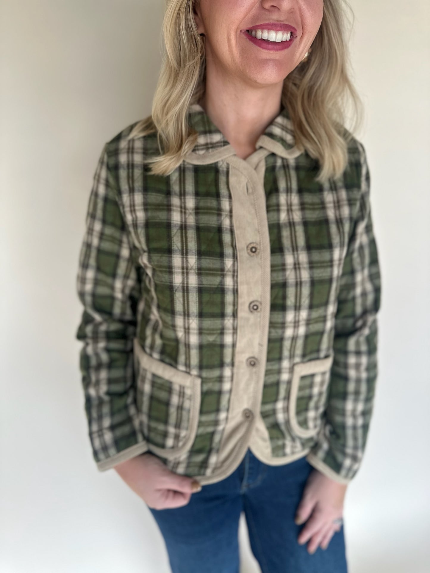 Close-up of green and tan plaid jacket featuring tan corduroy button placket, curved pockets, and collared neckline.