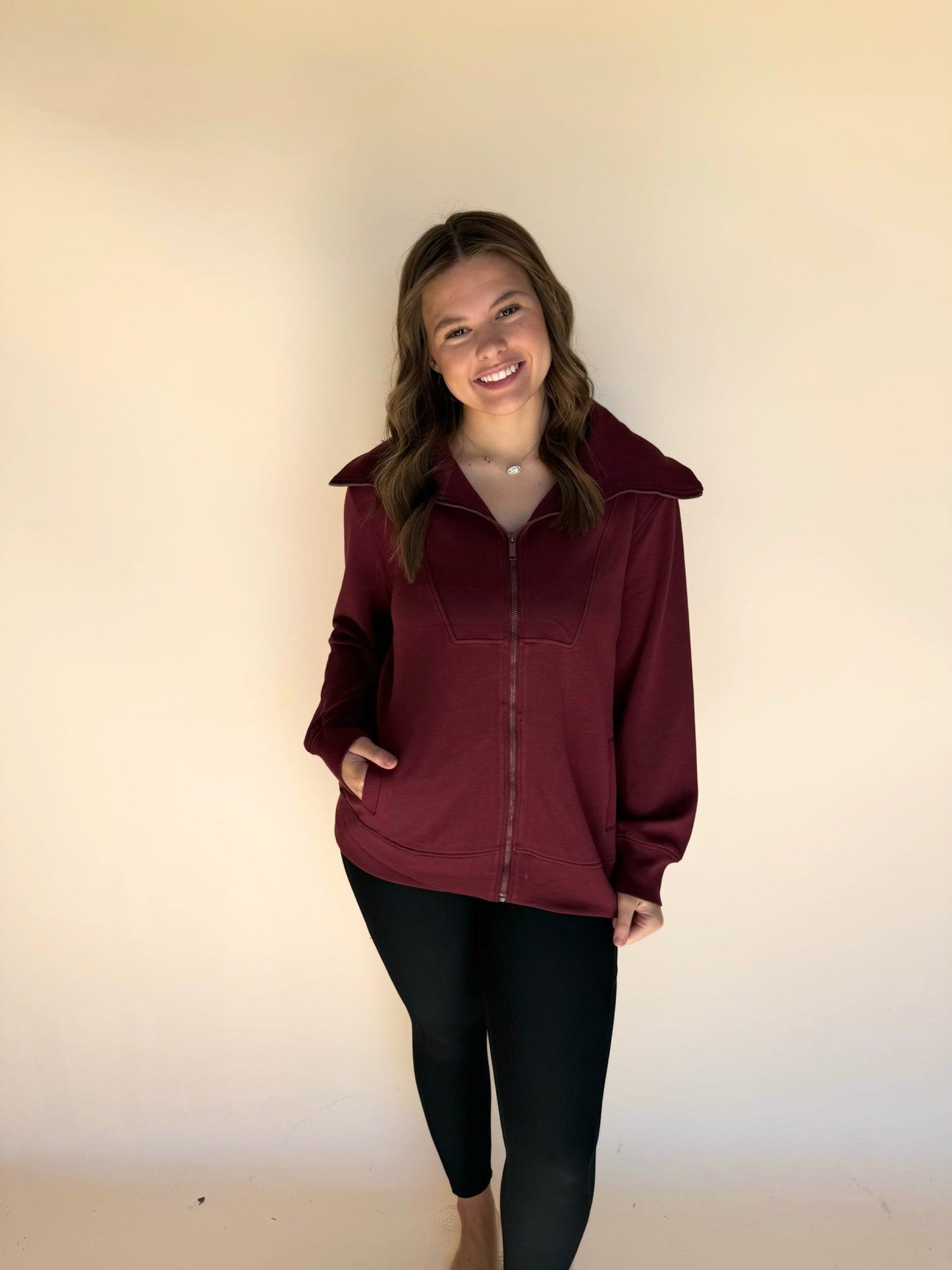 Woman wearing a burgundy jacket and black pants against a plain background