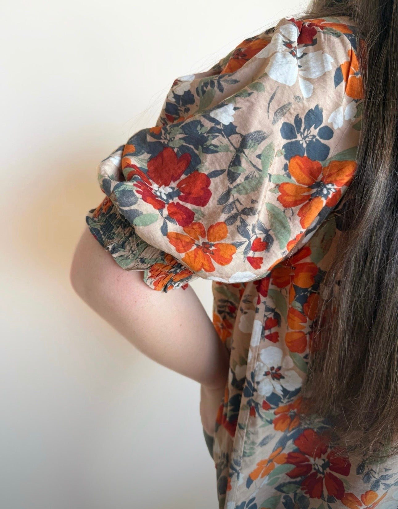 Close-up of short puff sleeve on a taupe floral top featuring rust, navy, white, and olive flowers with elastic cuff.