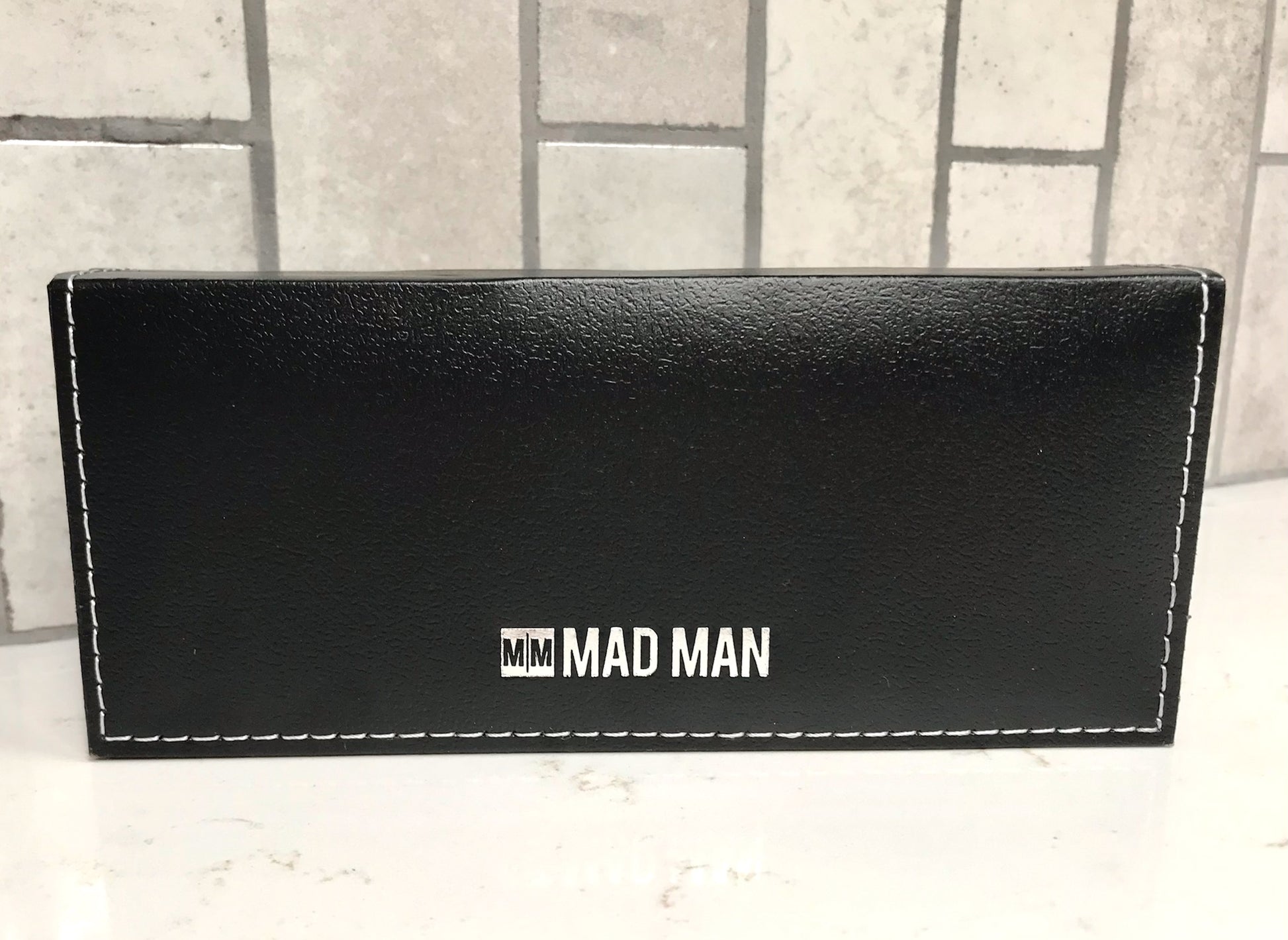 Black pen case with 'MM MAD MAN' branding on a light gray surface.