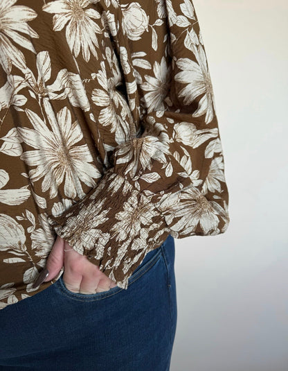 Close-up of smocked long sleeve on brown blouse with ivory floral print, paired with dark denim.