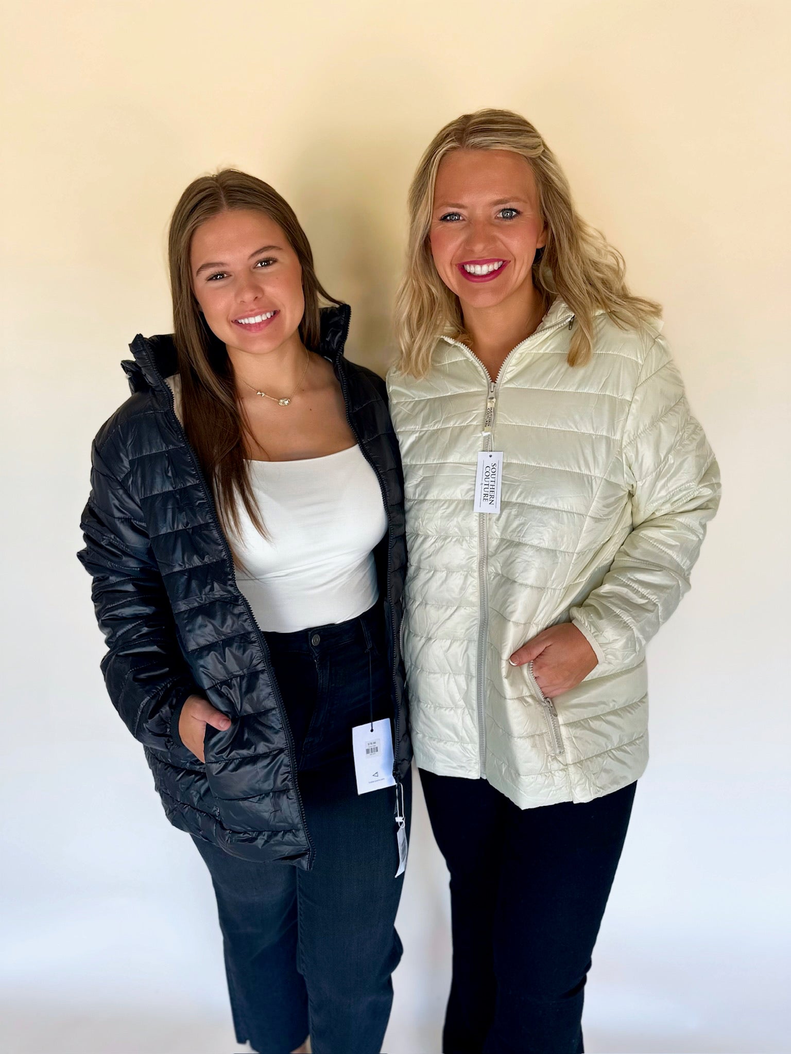 Two women wearing puffer jackets against a plain background