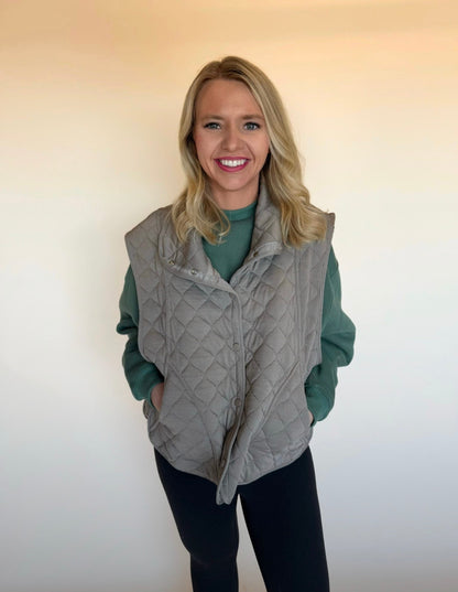 Woman wearing a quilted vest over a green shirt against a plain background