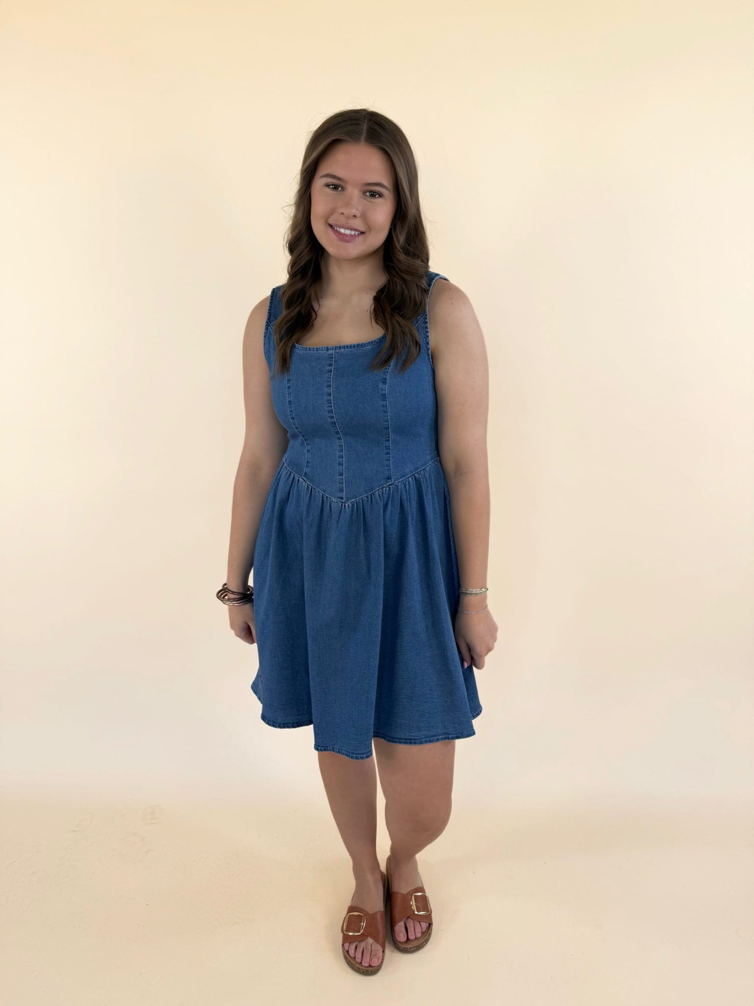 Woman wearing baby blue denim mini dress with scoop neckline and flowy skirt styled with brown sandals