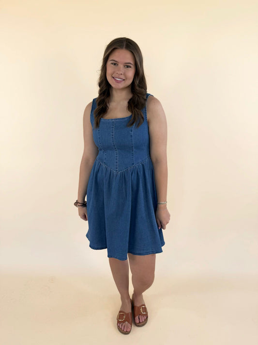 Woman wearing baby blue denim mini dress with scoop neckline and flowy skirt styled with brown sandals