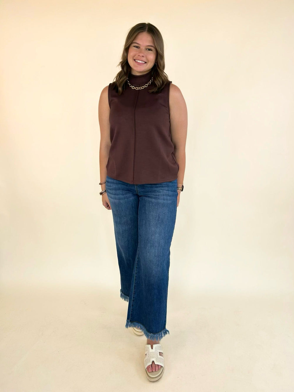 Women's brown mock neck sleeveless knit top paired with wide leg jeans.