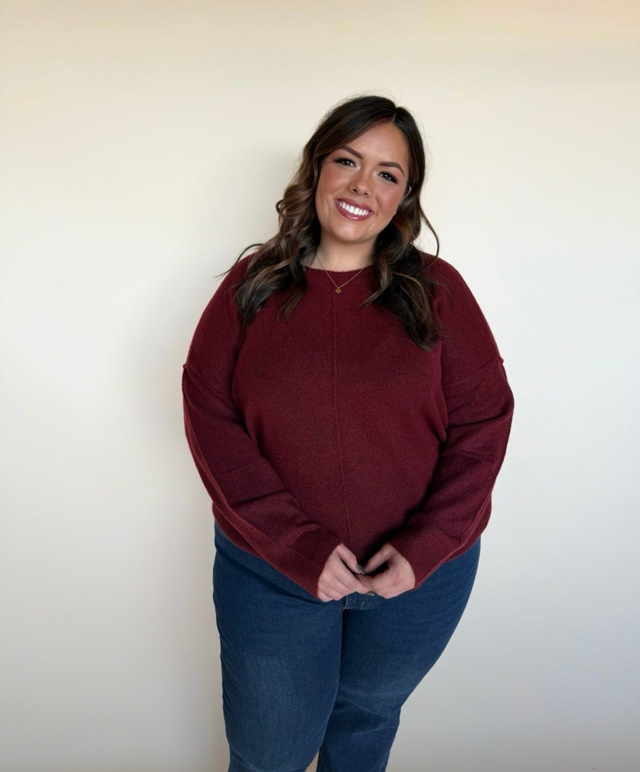 Woman wearing a maroon sweater and blue jeans against a plain background
