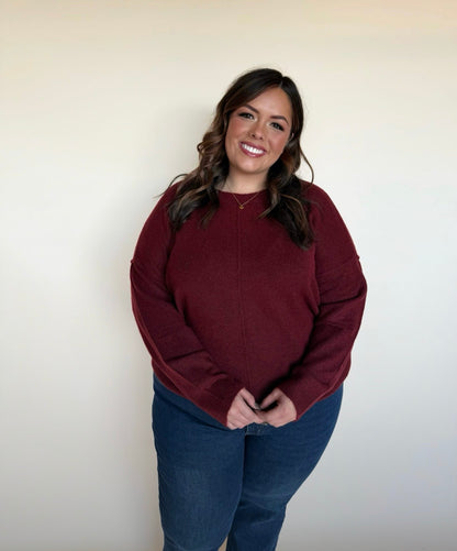 Woman wearing a maroon sweater and blue jeans against a plain background