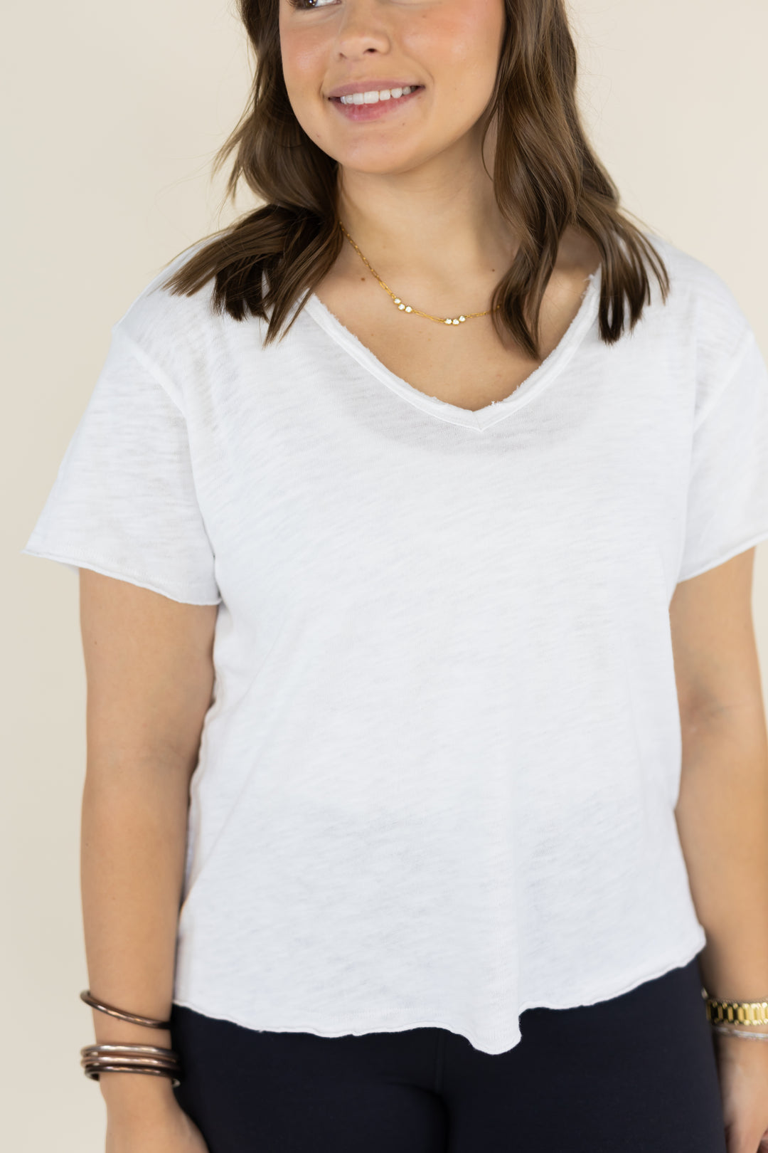 A woman wearing a white short-sleeve V-neck t-shirt with a slub texture, paired with dark pants, against a plain beige background.