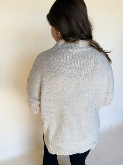 Back view of a cream mock-neck knit sweater with a soft textured finish, shown against a neutral background.