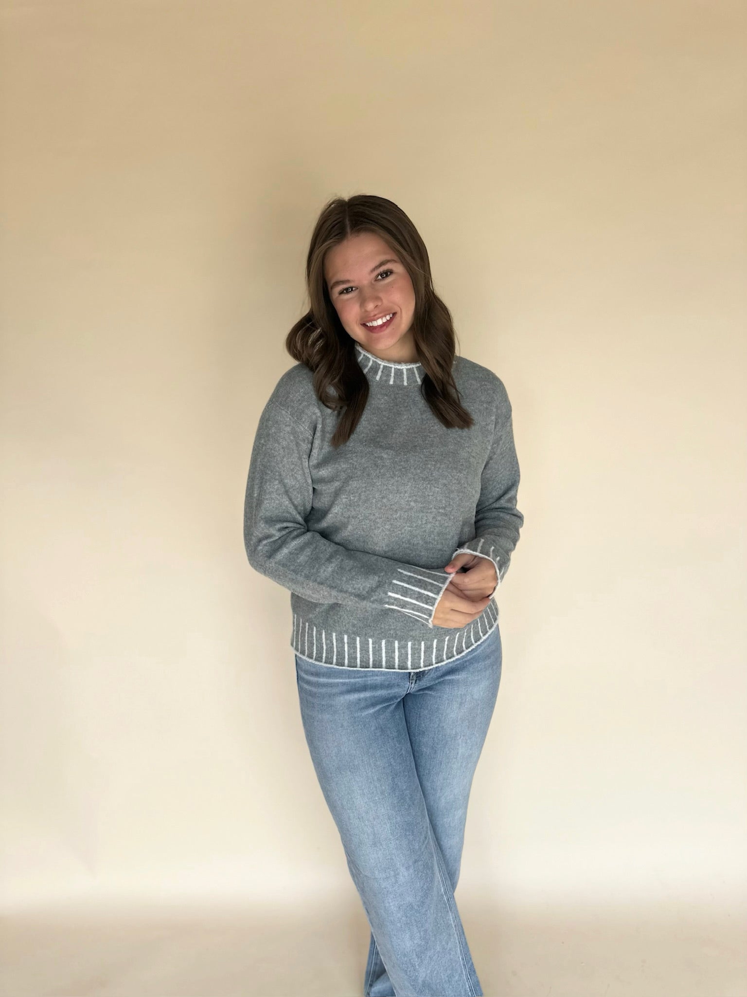 Woman wearing a light blue sweater and light blue jeans against a beige background