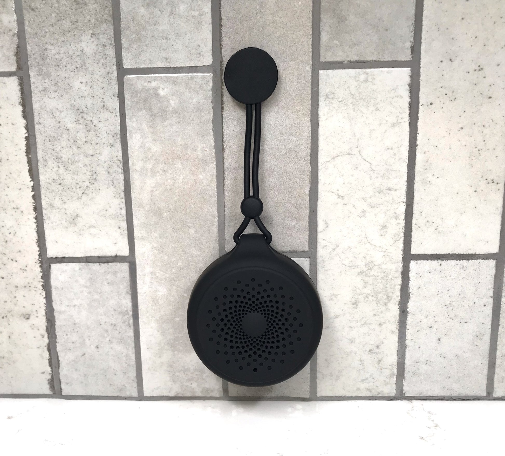 Black portable speaker with a lanyard on a tiled floor