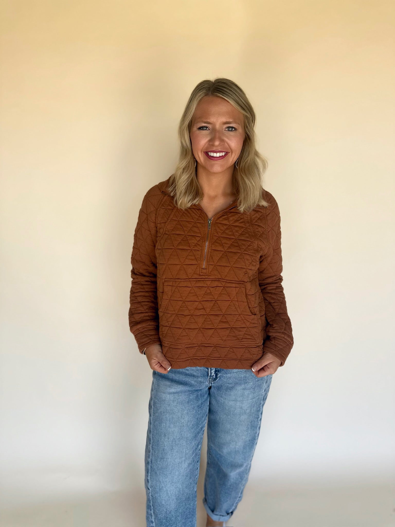 Woman wearing a copper quilted jacket and blue jeans against a plain background