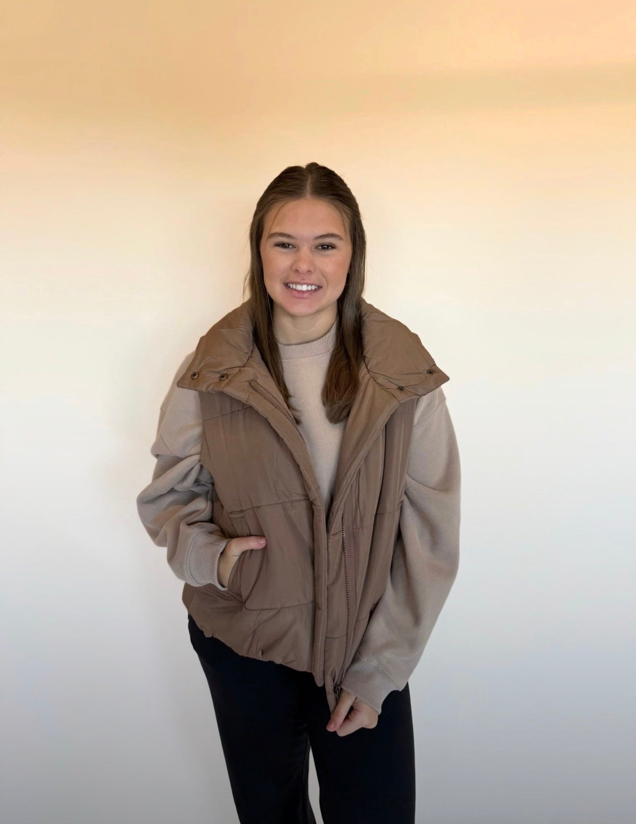 Person wearing a beige jacket with a hood against a plain background