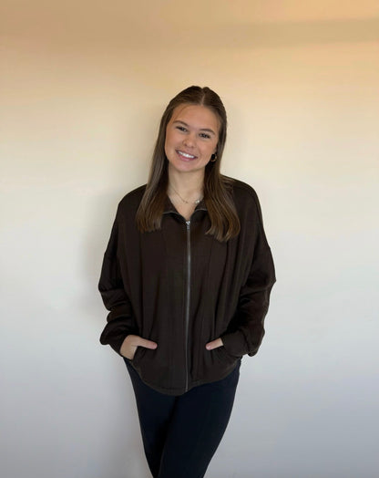 Person wearing a dark brown zip-up jacket against a plain background