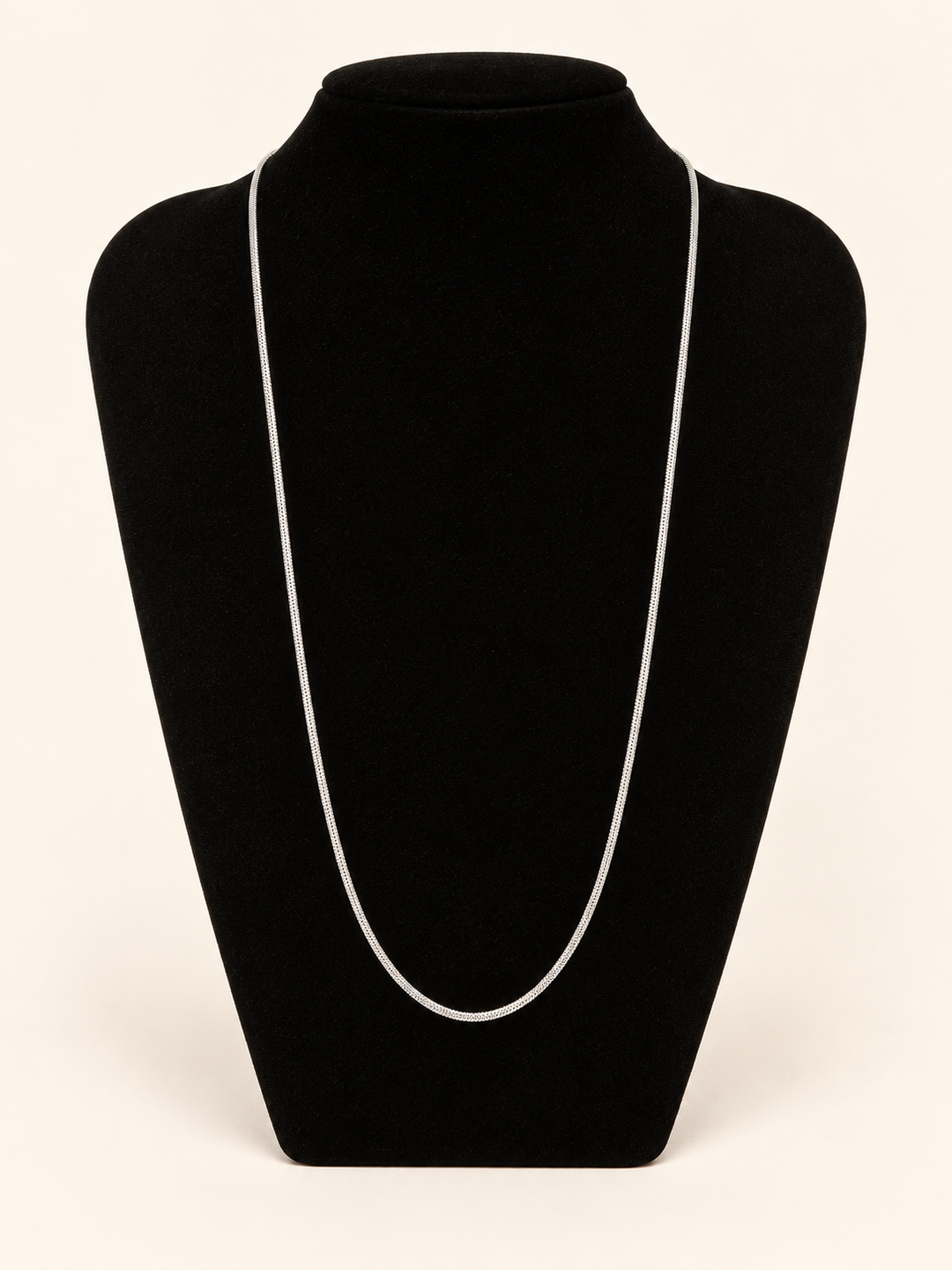 Long silver chain necklace displayed on a black velvet jewelry bust against a clean cream studio background.