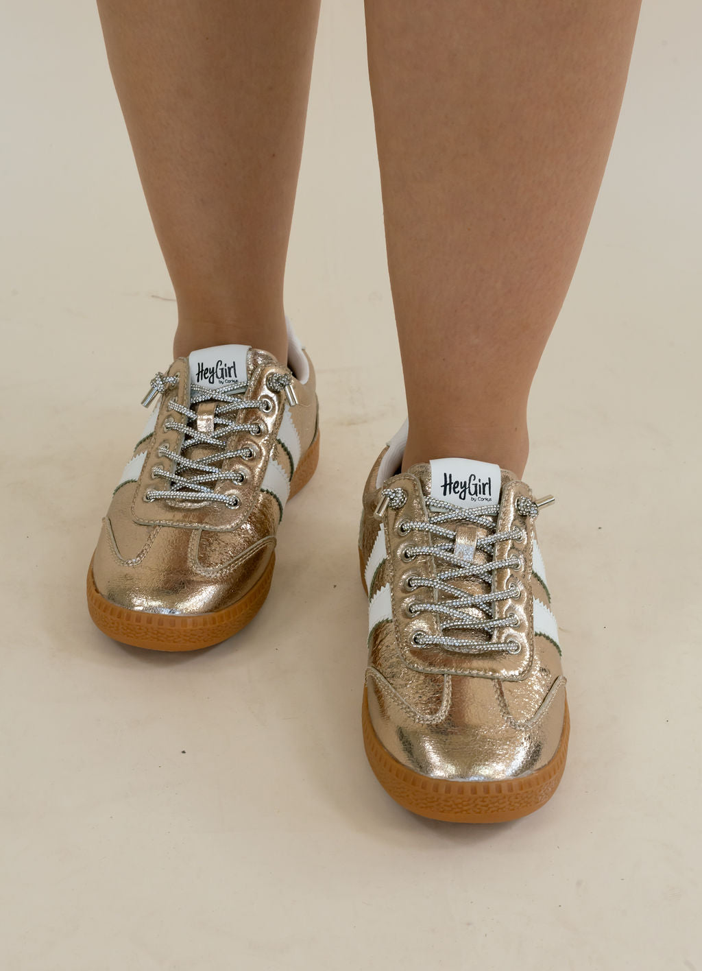 Metallic gold and white low-top sneakers with gum soles, shown on a person&