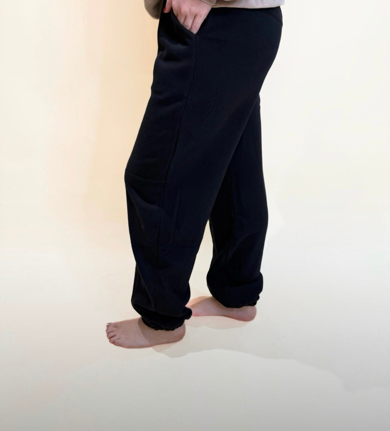 Side angle of black jogger pants with pockets and soft relaxed fit, elastic ankle cuffs and neutral background.