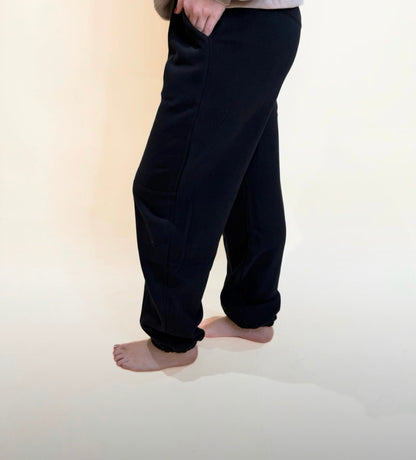 Side angle of black jogger pants with pockets and soft relaxed fit, elastic ankle cuffs and neutral background.