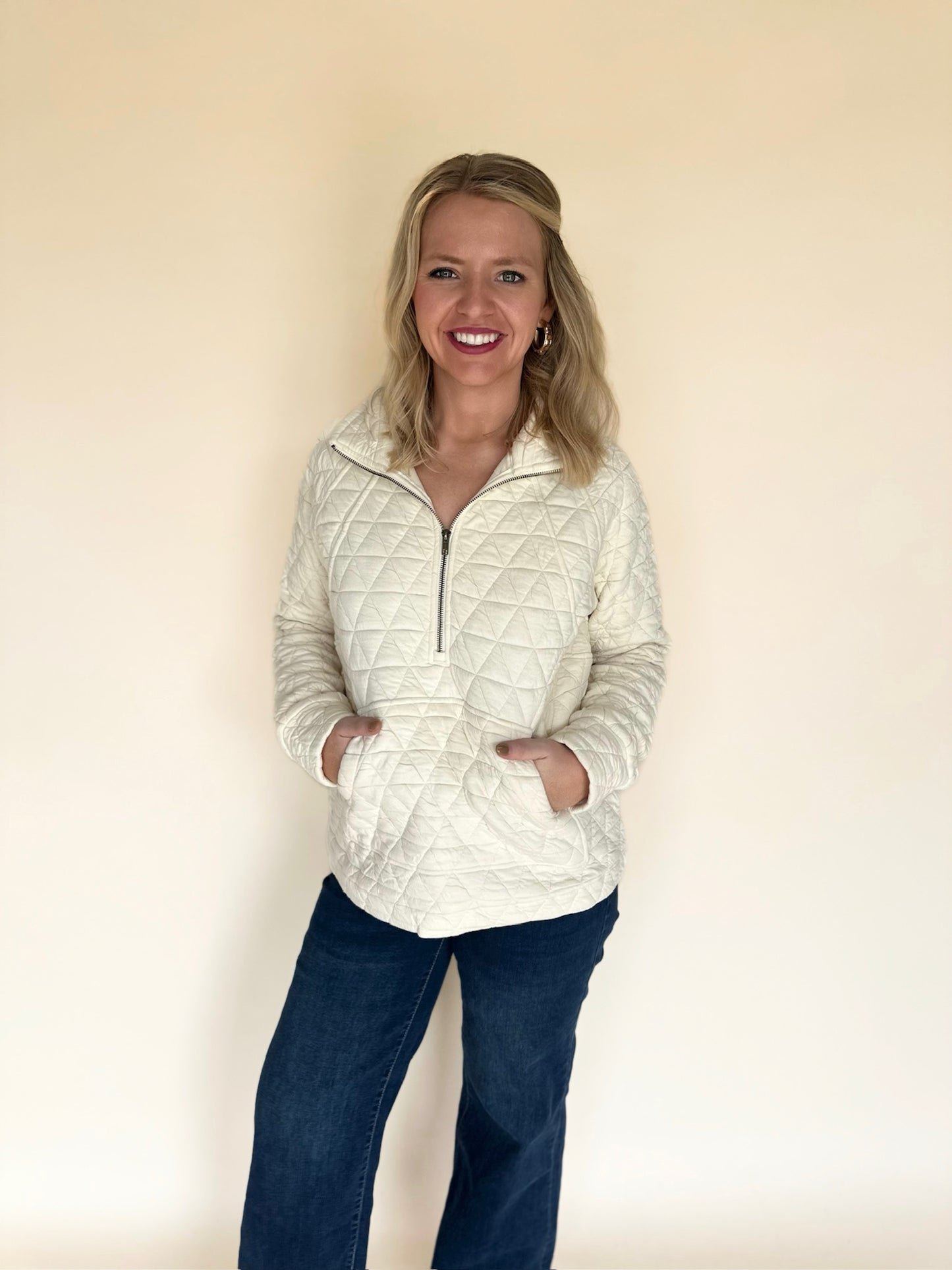 Woman wearing a quilted jacket and dark pants against a plain background