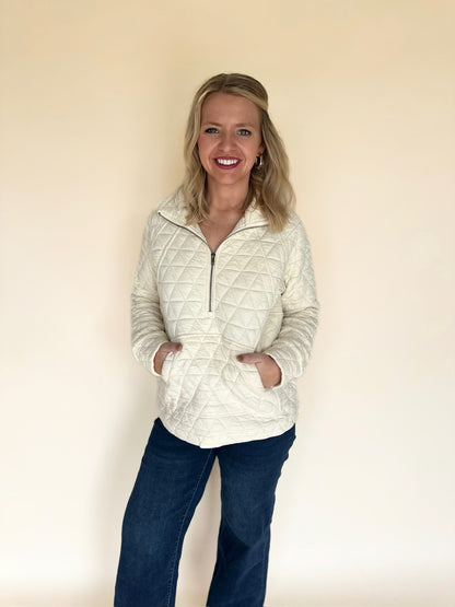 Woman wearing a quilted jacket and dark pants against a plain background