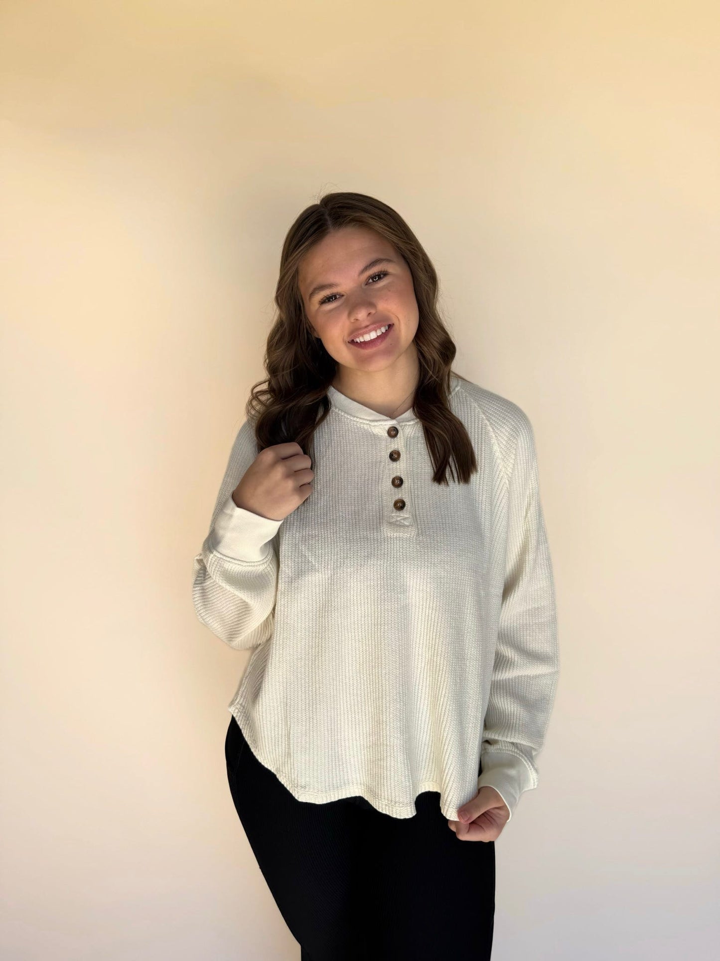 Woman wearing a cream long-sleeve shirt with buttons against a plain background