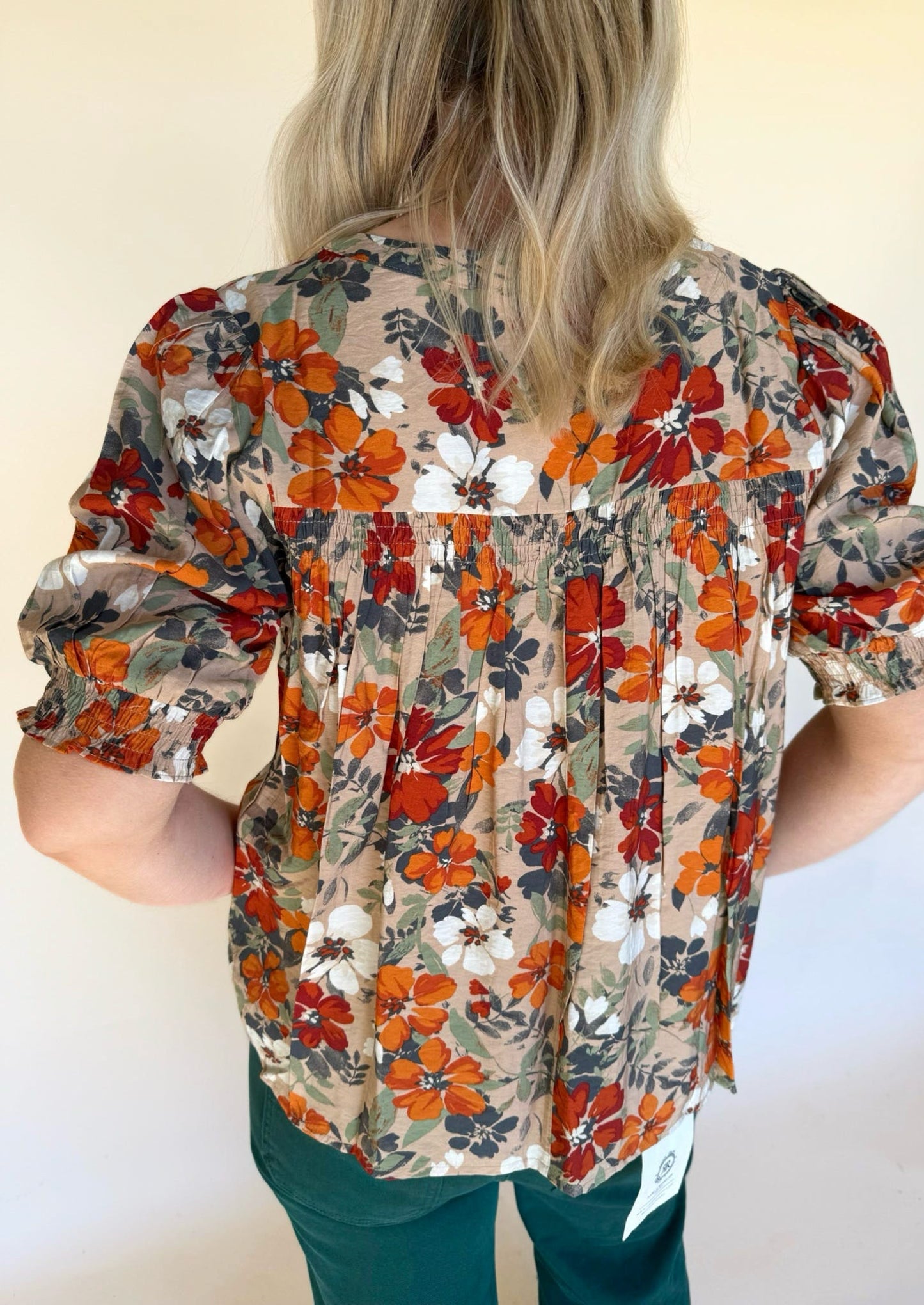 Back view of a fall floral blouse featuring smocked paneling and flowy fabric with orange, white, and navy flowers.