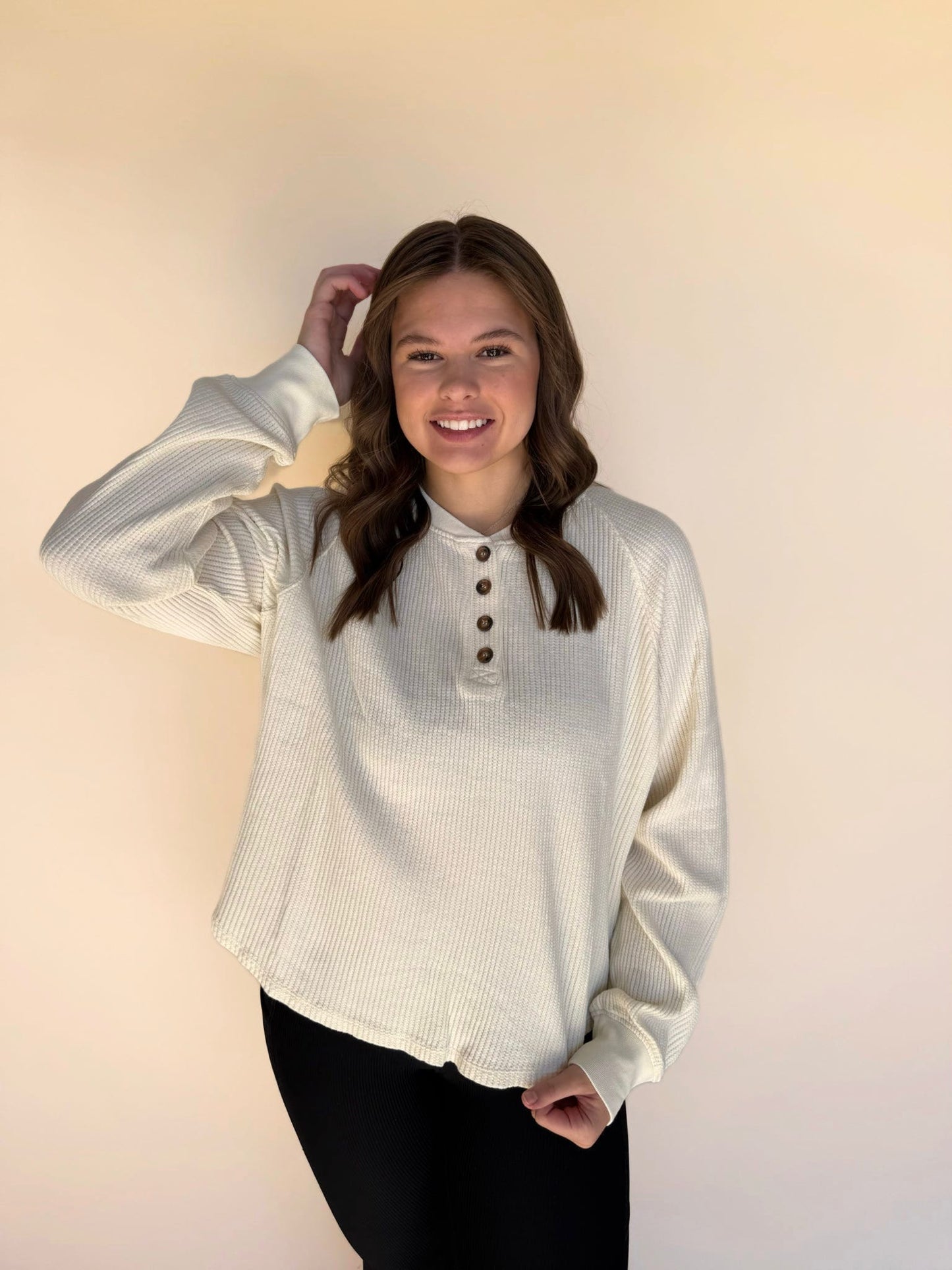Woman wearing a cream long-sleeve shirt with buttons against a plain background